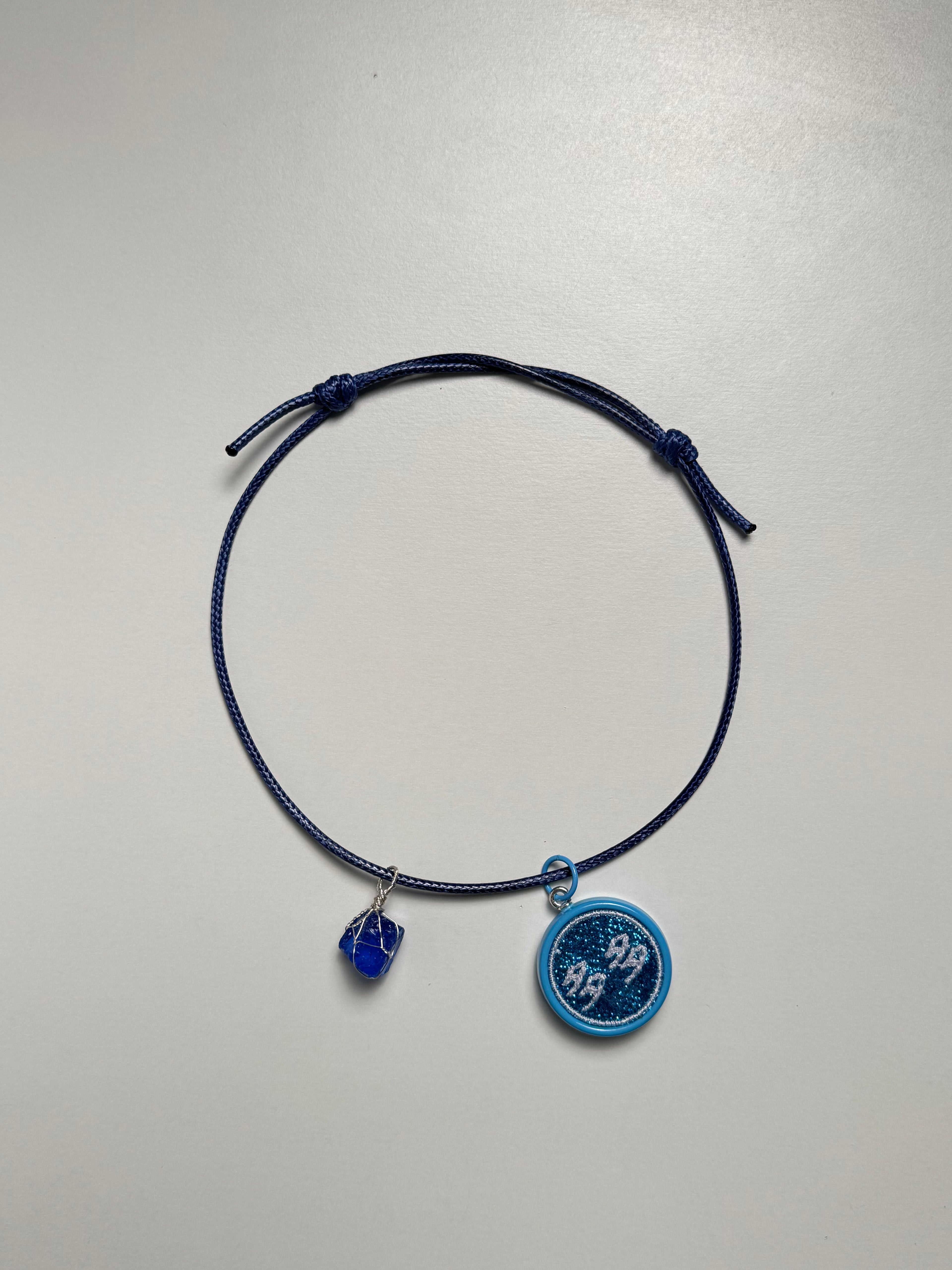 Navy blue cord bracelet with blue charms on a light gray background